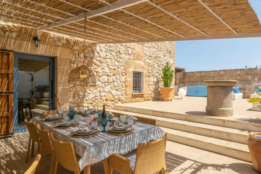 A shaded outdoor dining area with a set table beside a stone building and pool.