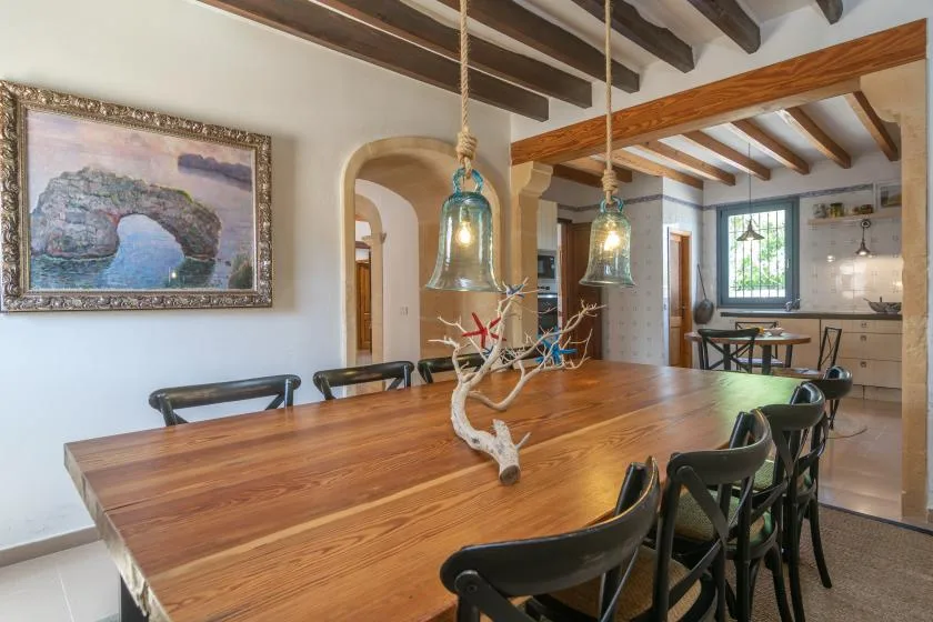 A dining area with a long wooden table and black seating beneath exposed ceiling beams.