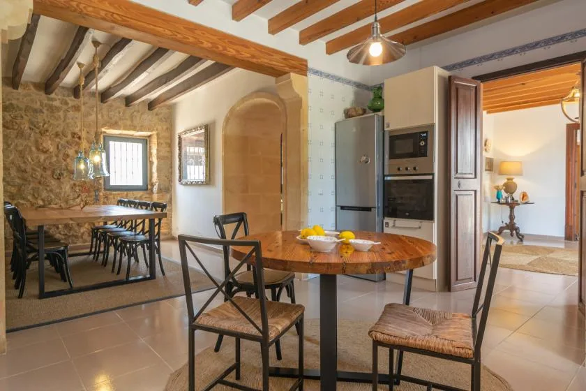 A dining area with a round table sits beside a stone-walled kitchen.