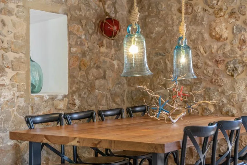 A dining area with a long wooden table, chairs, and hanging lights.