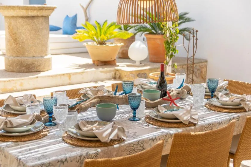 A sunlit dining area with a table set for a meal and potted plants nearby.