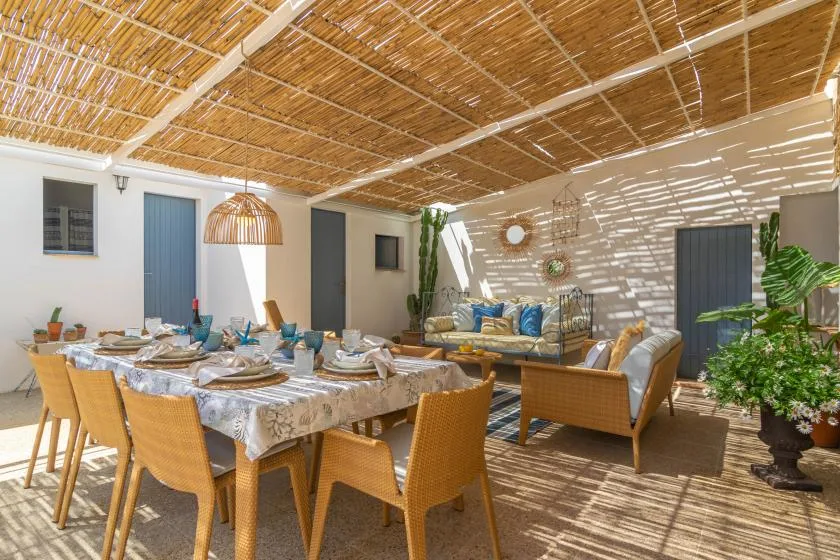 A shaded outdoor dining and seating area with a long table and woven chairs.