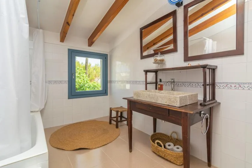 A bright bathroom with a wooden vanity, mirrors, and a window overlooking greenery.