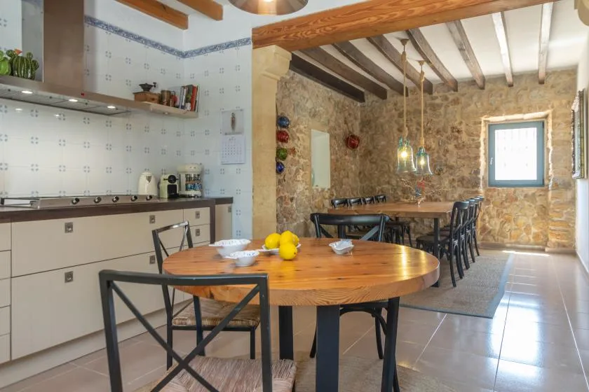 A dining area with a large wooden table, chairs, and a stone wall.