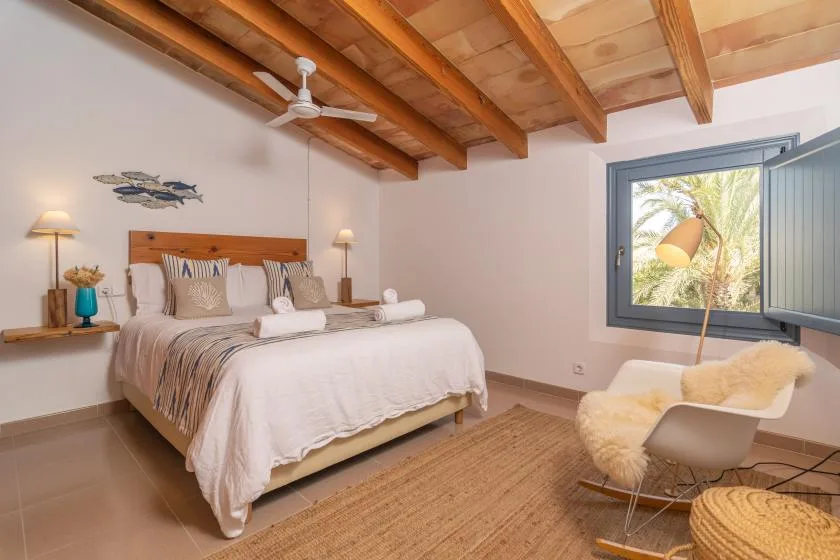 A bedroom with a neatly made bed, exposed wooden ceiling beams, and a window.