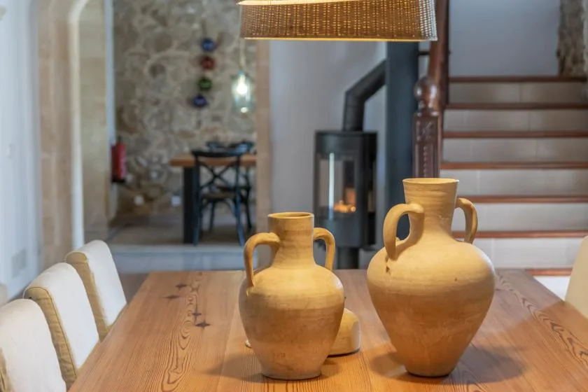 A dining table with ceramic vessels sits in front of a staircase and stone wall.