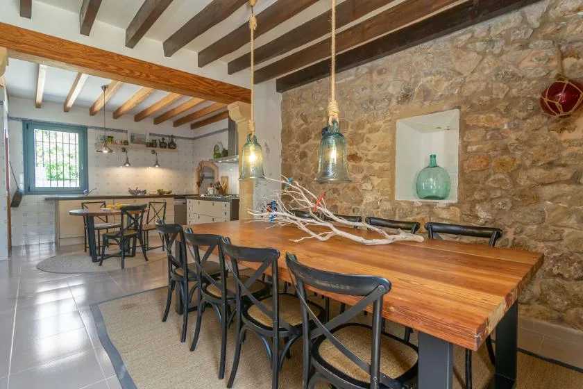 A dining area with a long wooden table and an open kitchen in the background.