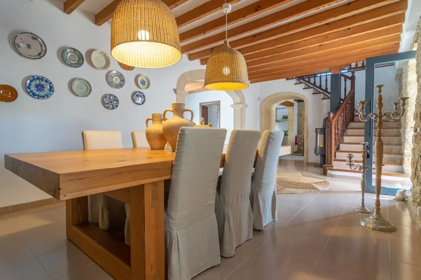 A dining area with a wooden table, upholstered seating, and hanging lights.