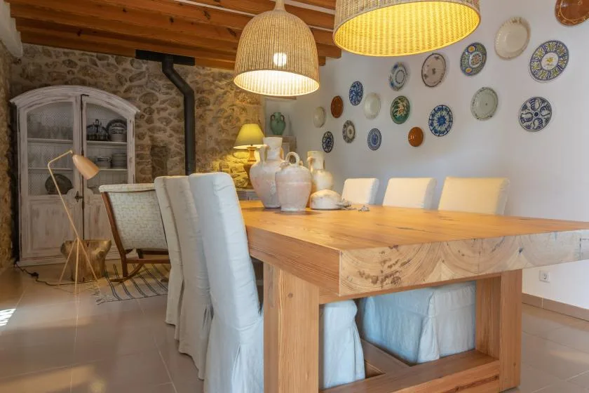 A dining area with a long wooden table, light chairs, and decorative plates on the wall.