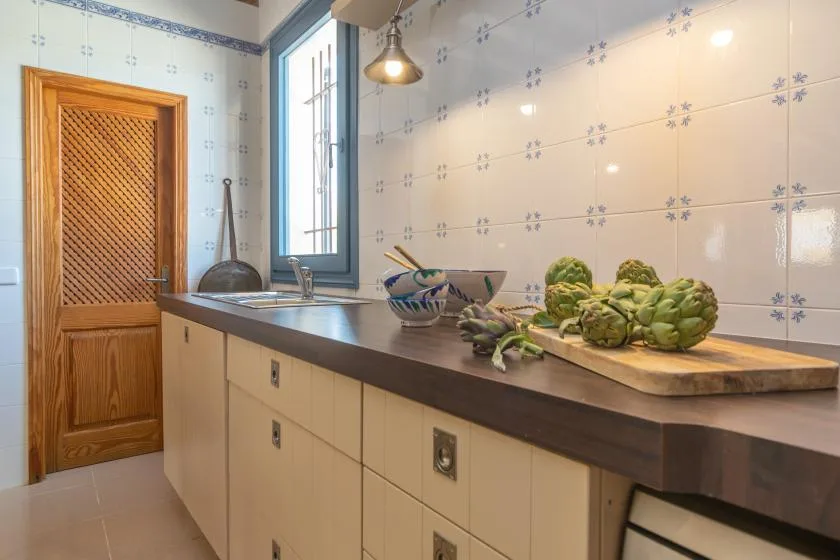 A tiled kitchen counter holds a bowl and fresh artichokes beside a window.