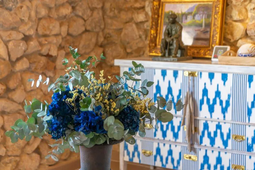 A floral arrangement sits beside a blue-and-white tiled cabinet against a stone wall.