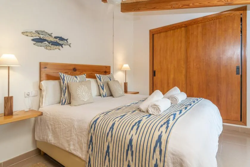 A bedroom with a neatly made bed, patterned pillows, and wooden doors.