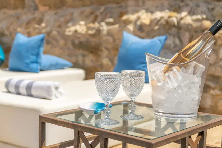 A patio seating area with blue cushions and a glass table holding drinks.