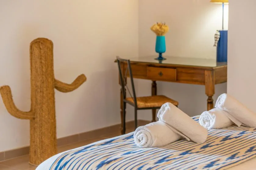 A bedroom with a striped bed, rolled towels, and a wooden desk.