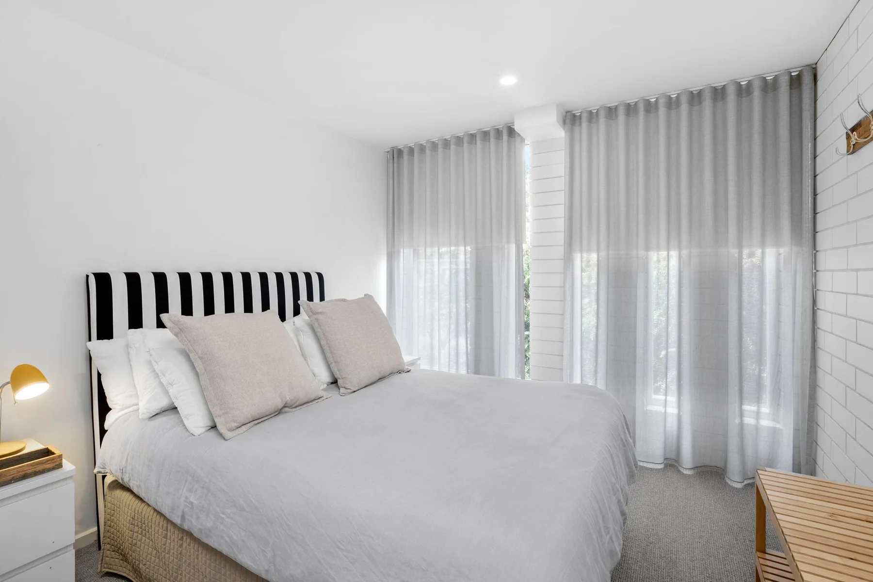 A bedroom with a bed dressed in light bedding beside tall curtained windows.