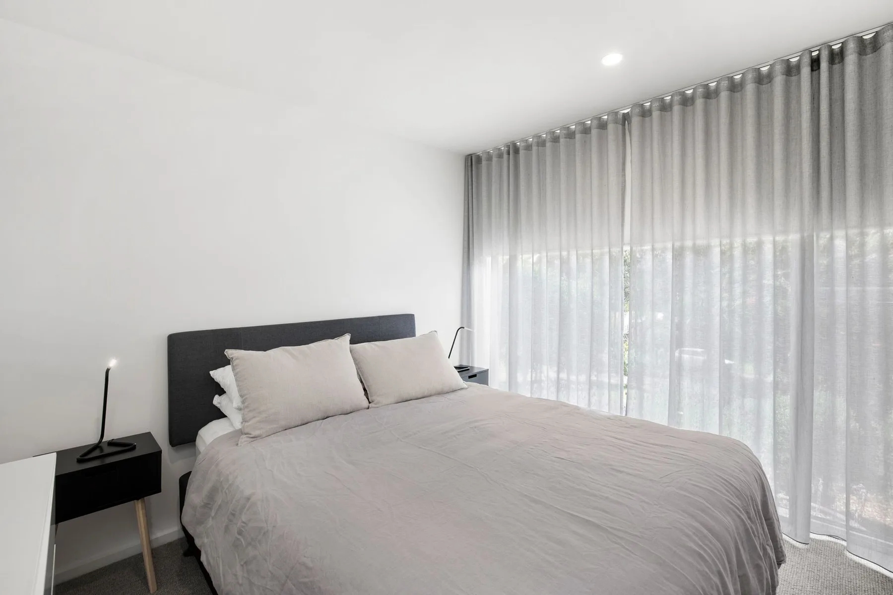 A bedroom with a neatly made bed and full-length curtains.
