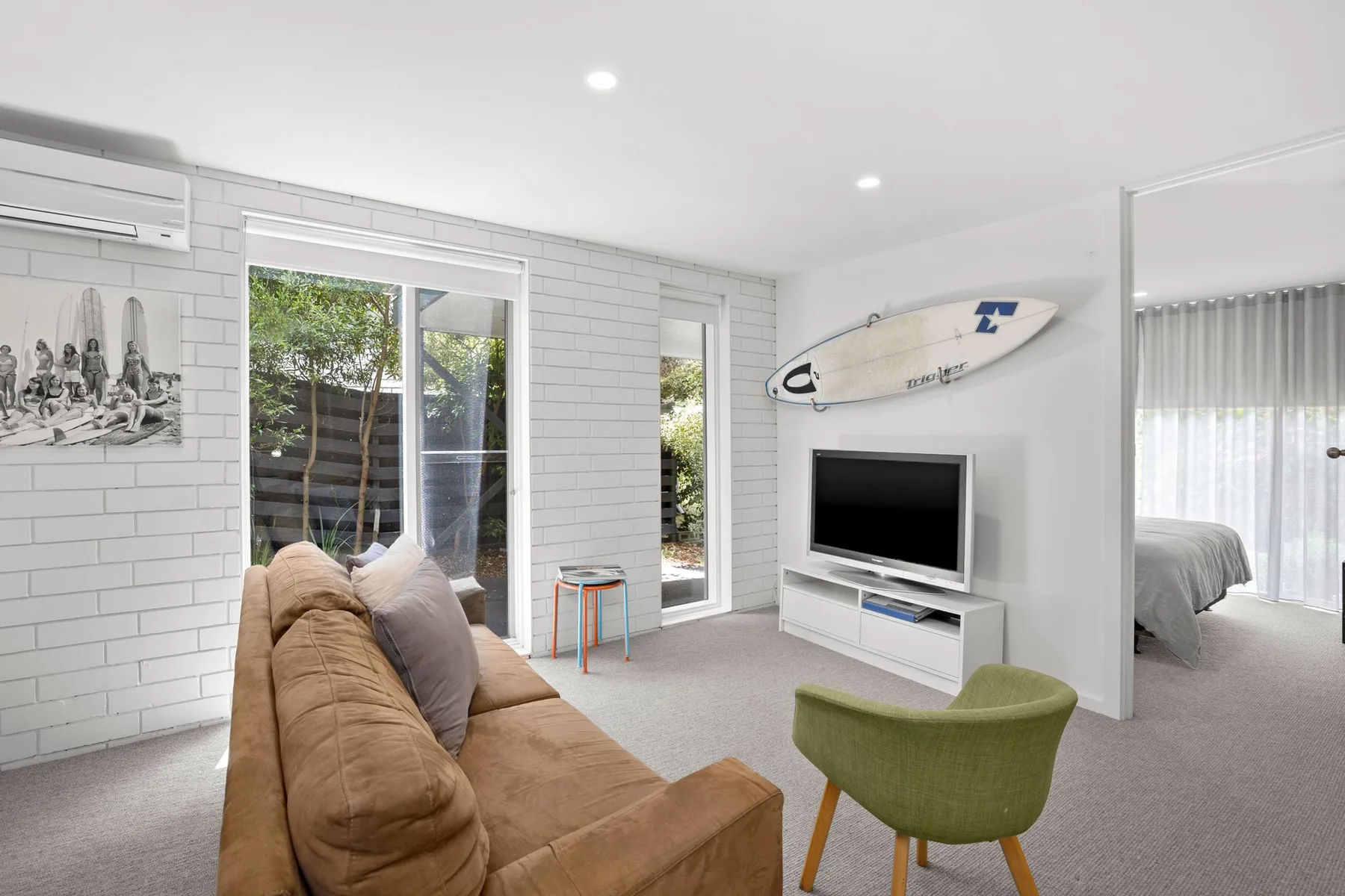 A bright living room with a sofa, television, and large windows.
