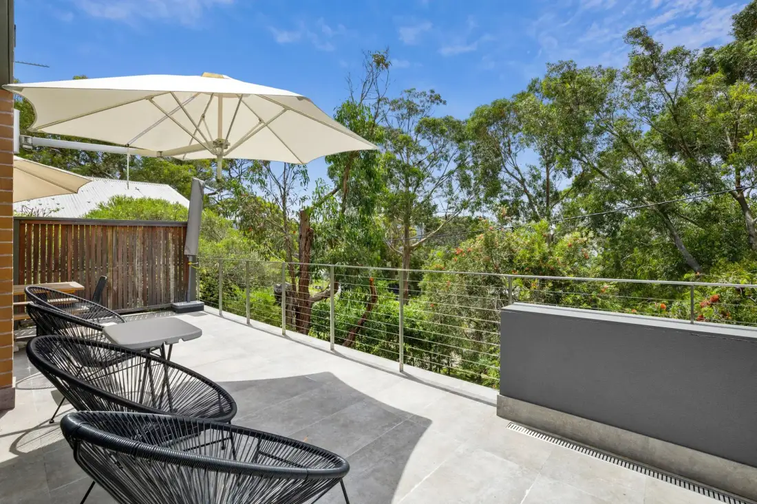 A sunny outdoor terrace with seating, an umbrella, and views of surrounding trees.