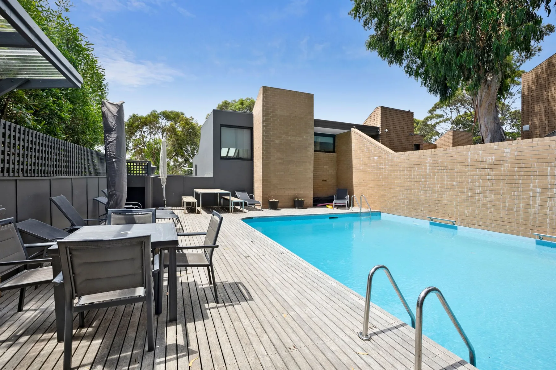 An outdoor swimming pool beside a wooden deck with dining seating.