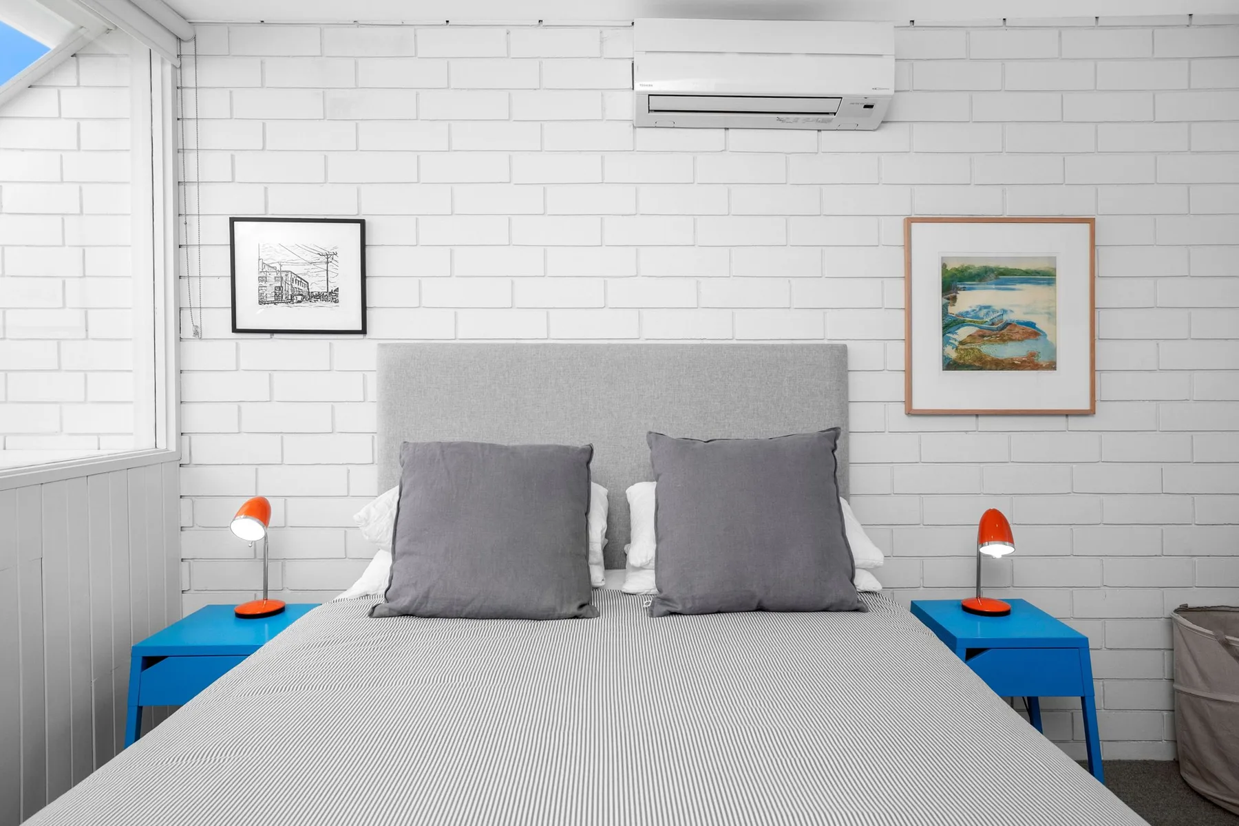 A bedroom with a neatly made bed, blue bedside tables, and framed artwork.