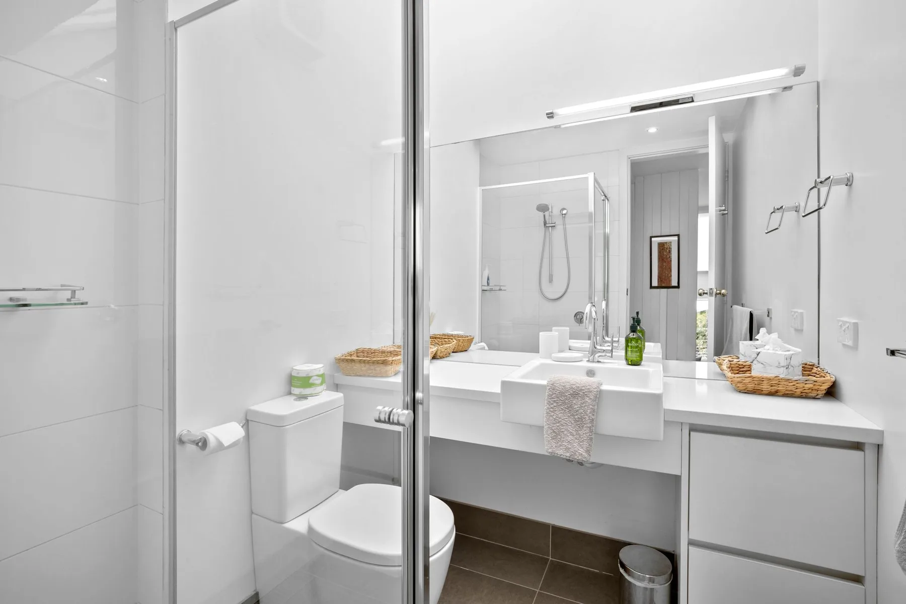 A bright bathroom with a sink vanity, mirror, and shower.