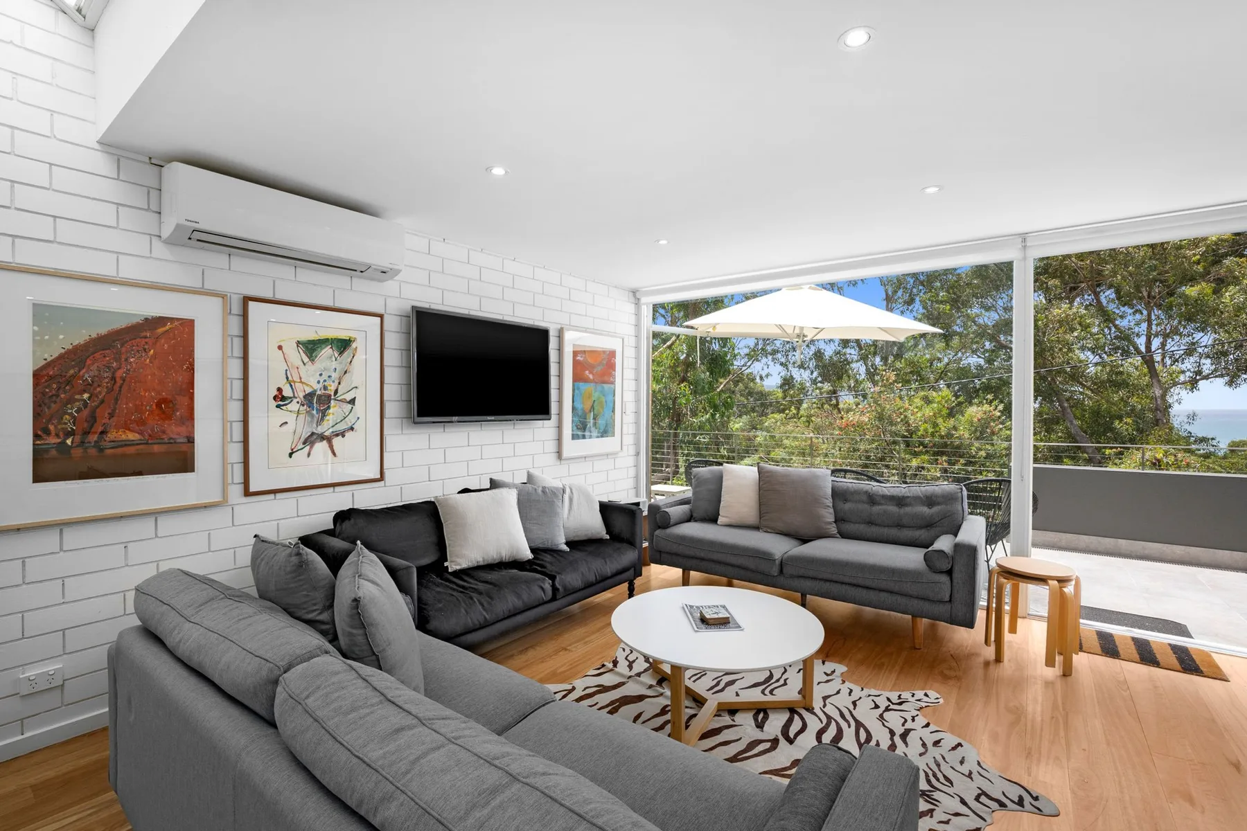 A bright living room with gray seating, framed art, and large windows.