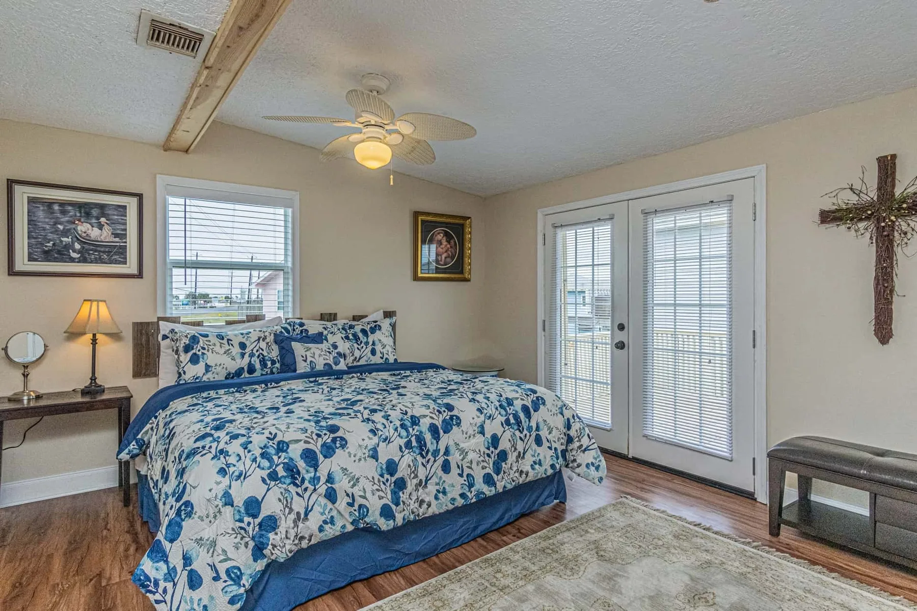 A bedroom with a blue floral bedspread, windows, and glass doors.