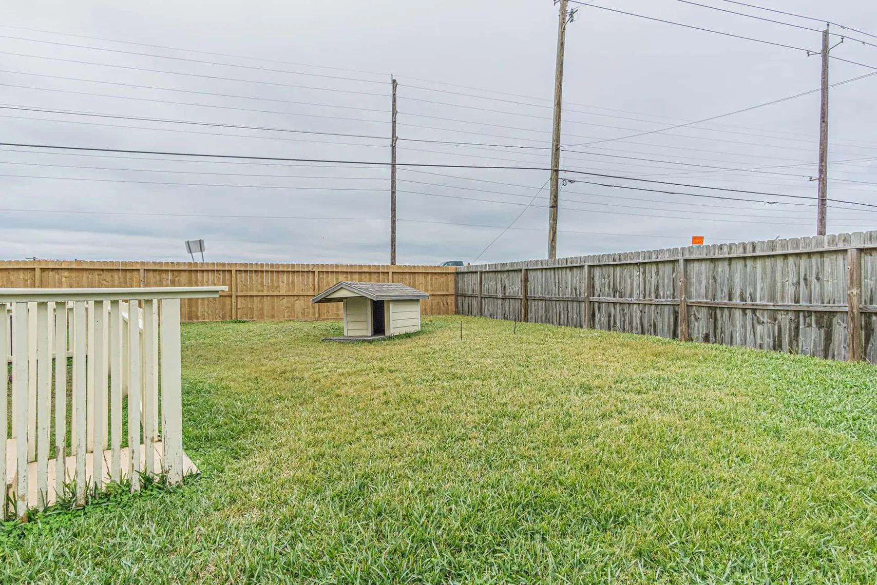A grassy fenced yard with a small covered structure near the back.
