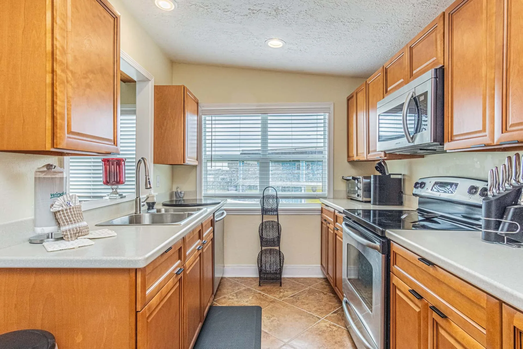 A kitchen with wooden cabinets, counters, and a window with blinds.