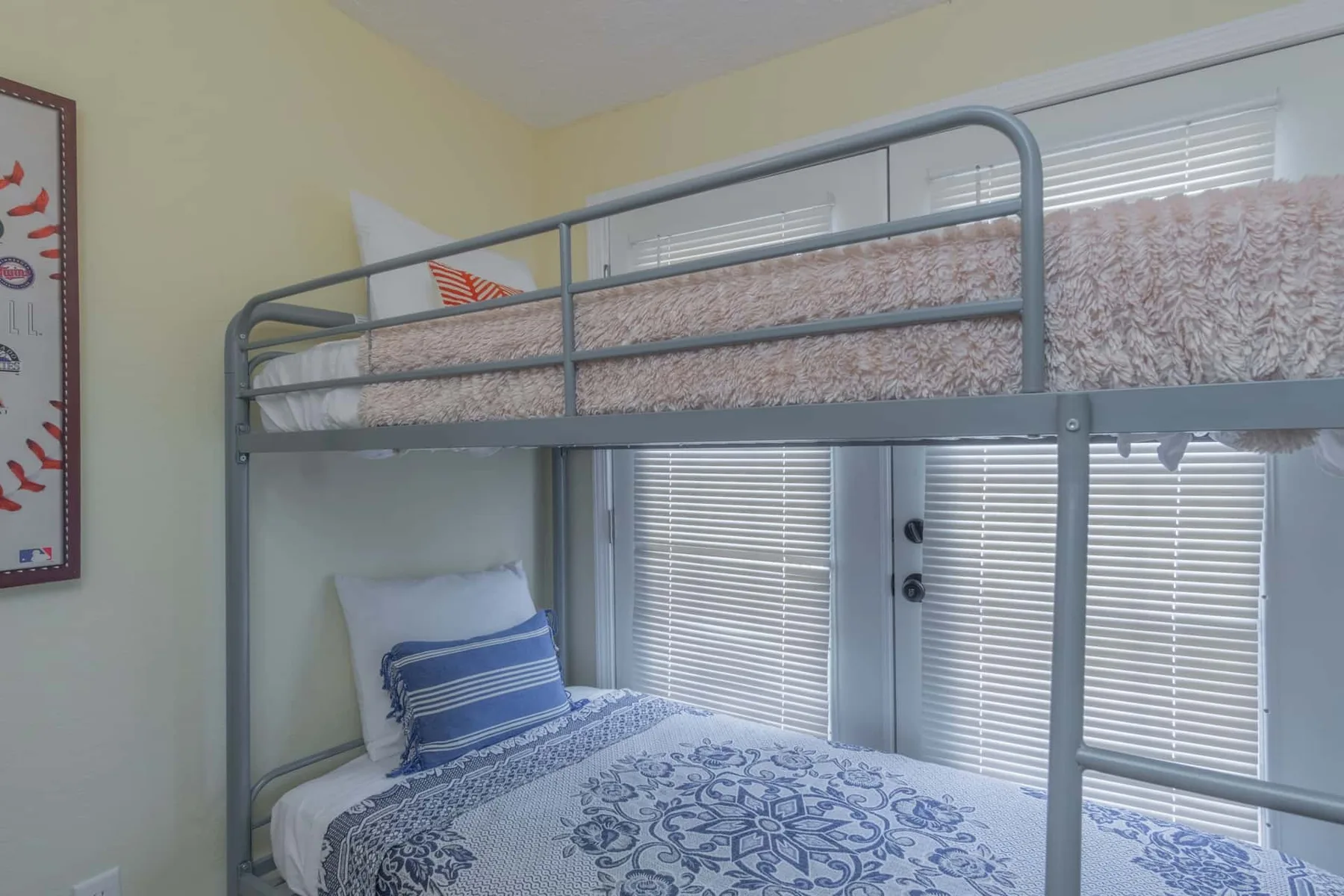 A bedroom with a metal bunk bed, patterned bedding, and window blinds.