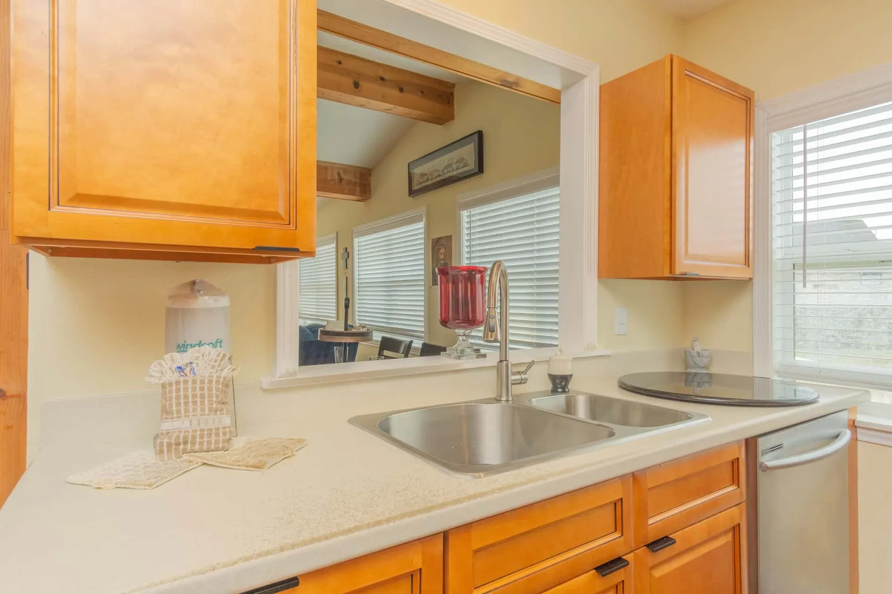 A kitchen counter with a double sink, wooden cabinets, and windows.