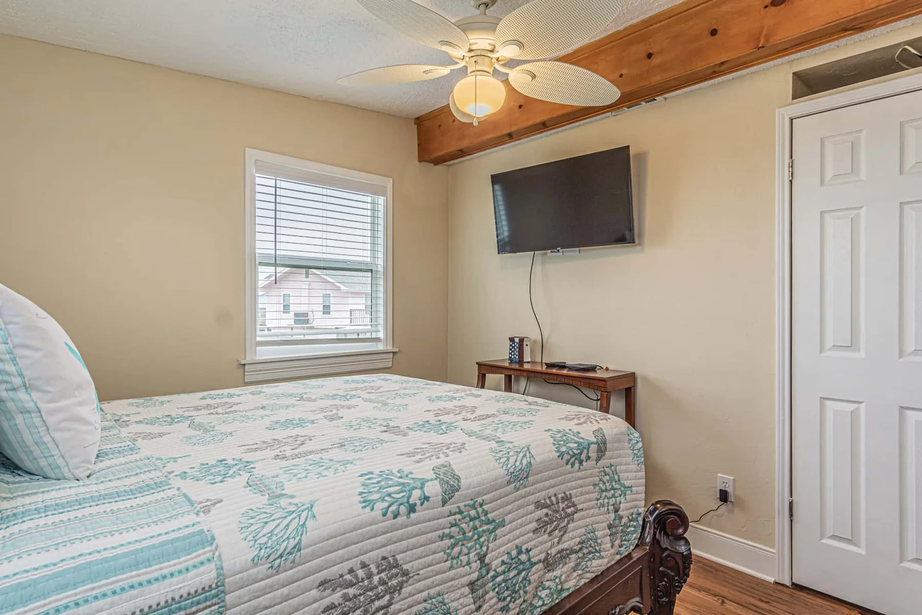 A bedroom with a patterned bed, a window, and a wall-mounted television.