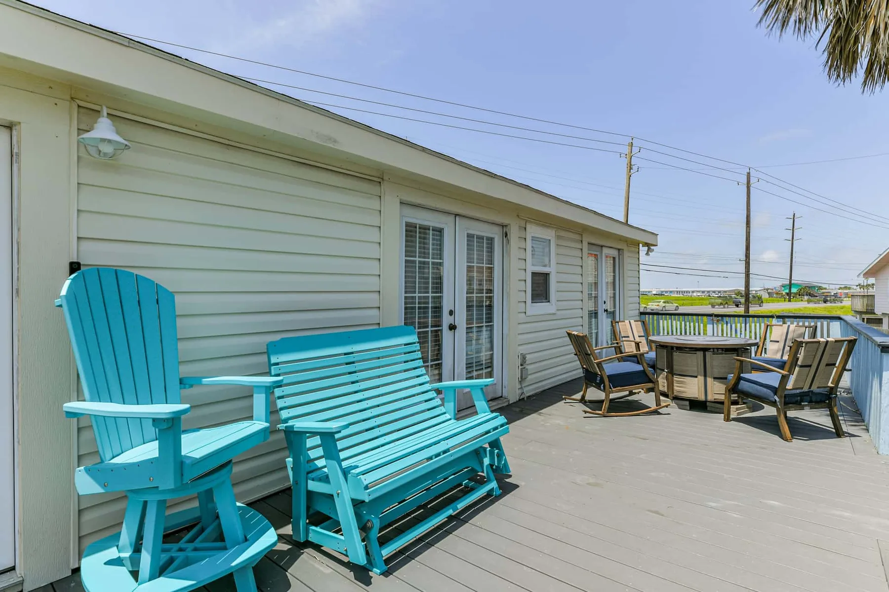 An outdoor deck beside a light-colored building, furnished with turquoise seating and a dining table.