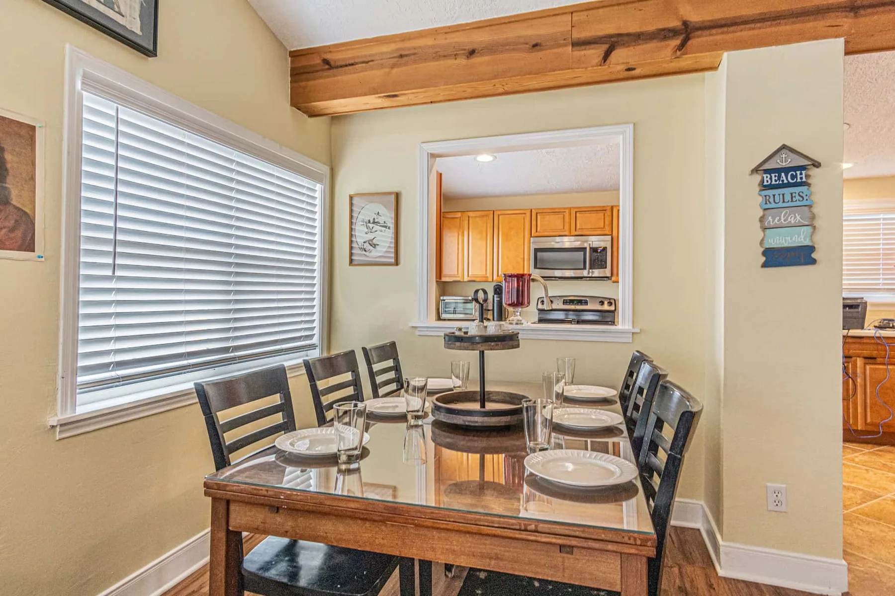 A dining area with a glass-topped table and a kitchen visible through an opening.
