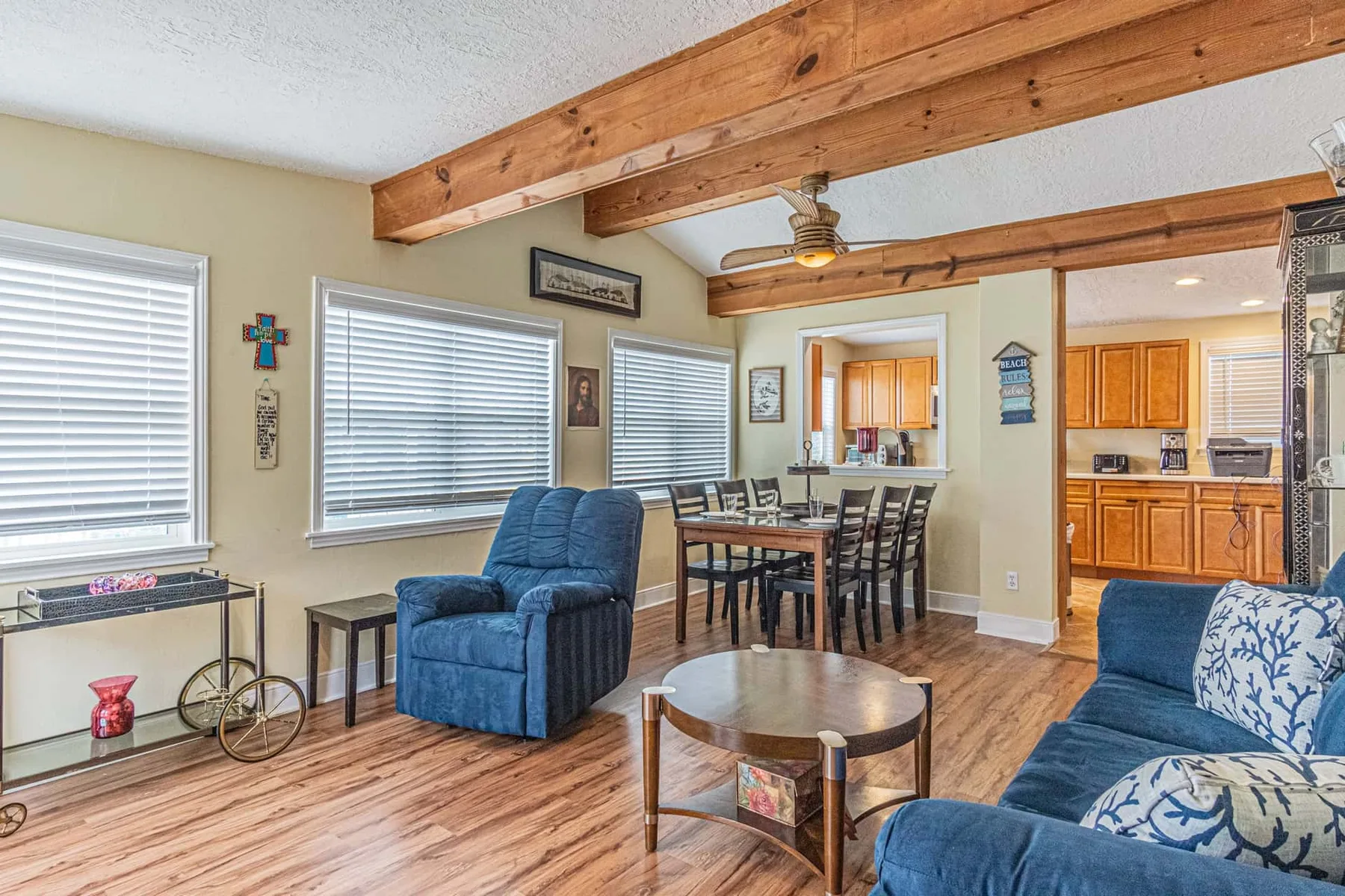 A living and dining area with blue seating, a dining table, and exposed wooden beams.