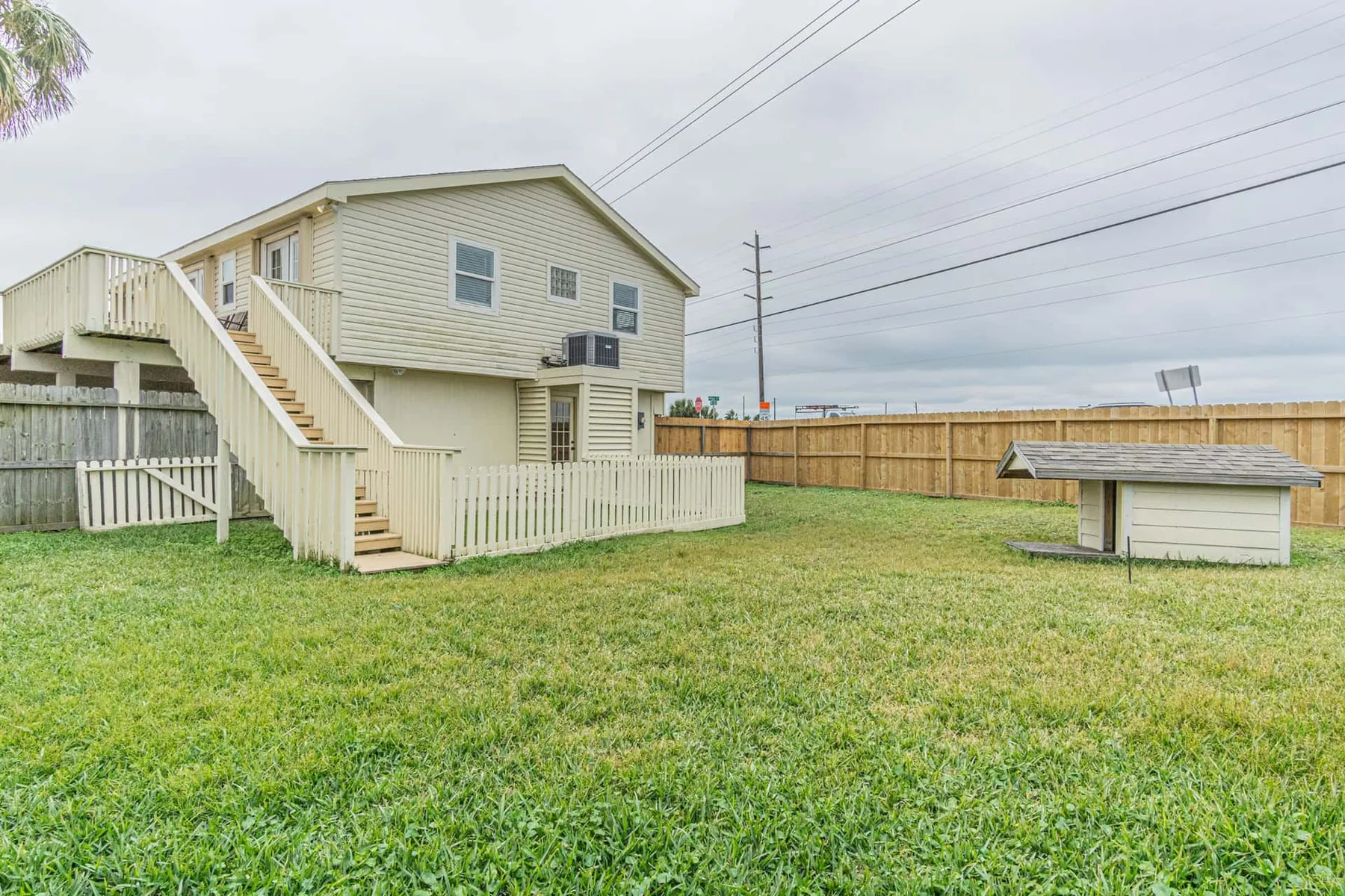A raised house stands beside a grassy yard and a fenced outdoor area.