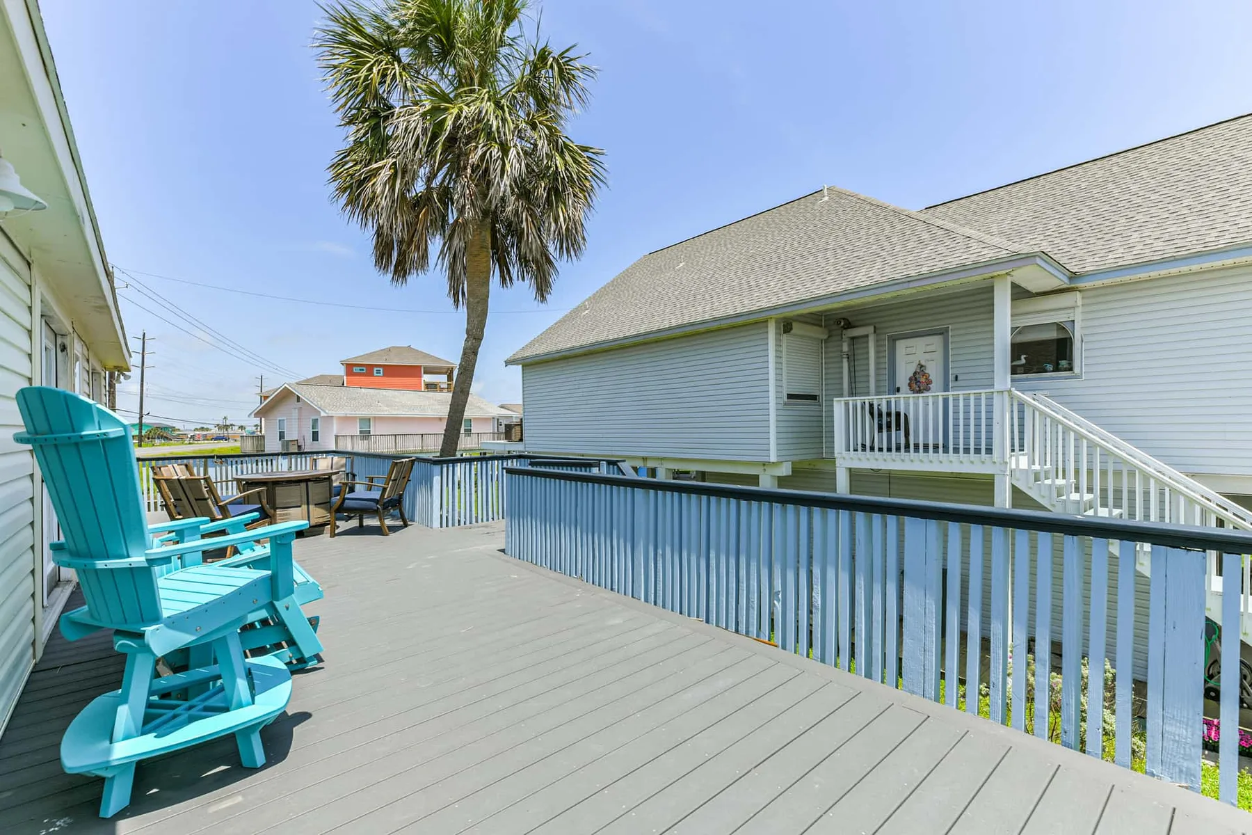 A raised outdoor deck with blue seating overlooks nearby houses and a palm tree.