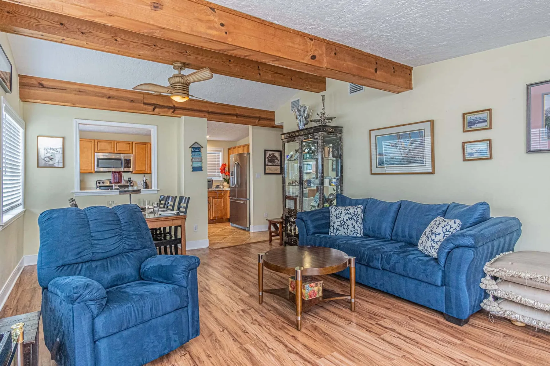 A living room with blue seating, a coffee table, and exposed wooden ceiling beams.