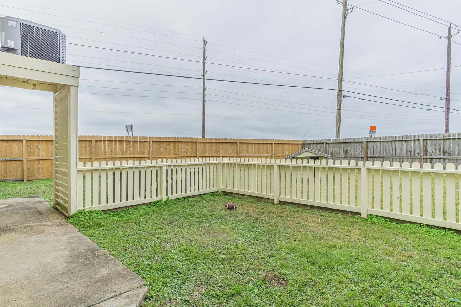 A fenced outdoor yard with a grassy area and a concrete walkway.