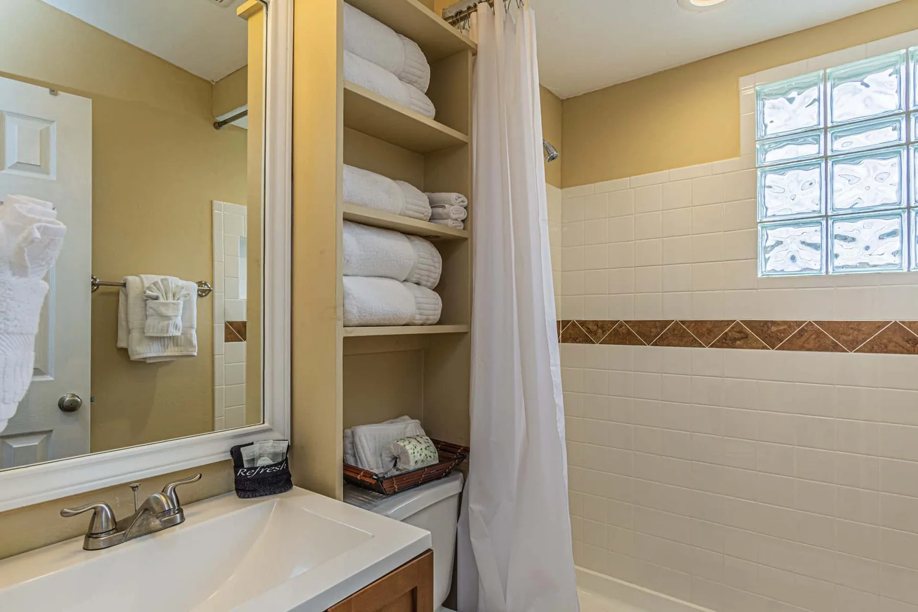 A bathroom with a sink, open towel shelves, and a curtained shower.