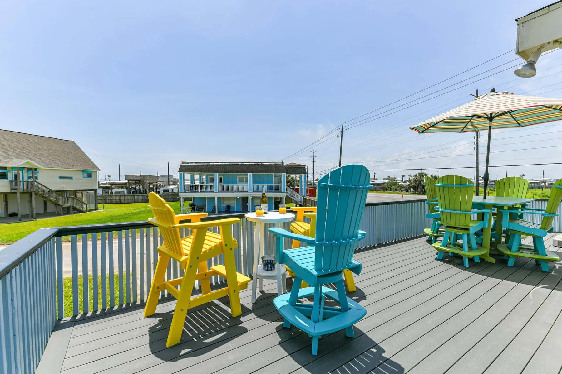 An outdoor deck has colorful seating and a striped umbrella overlooking the water.