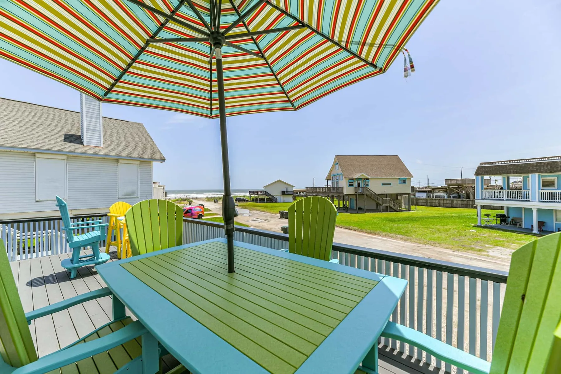 A deck dining area with colorful striped umbrella and green seating overlooks the water.