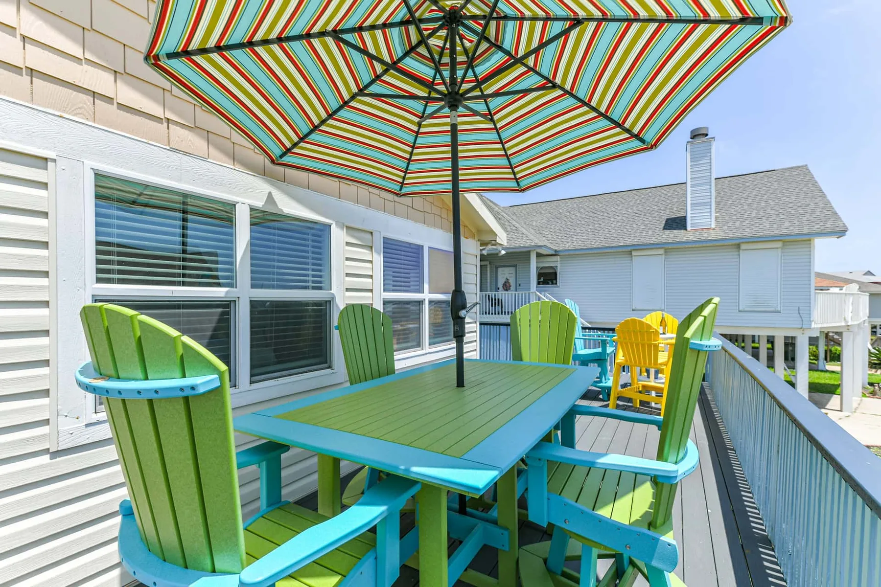 An outdoor deck has colorful seating around a table beneath a striped umbrella.