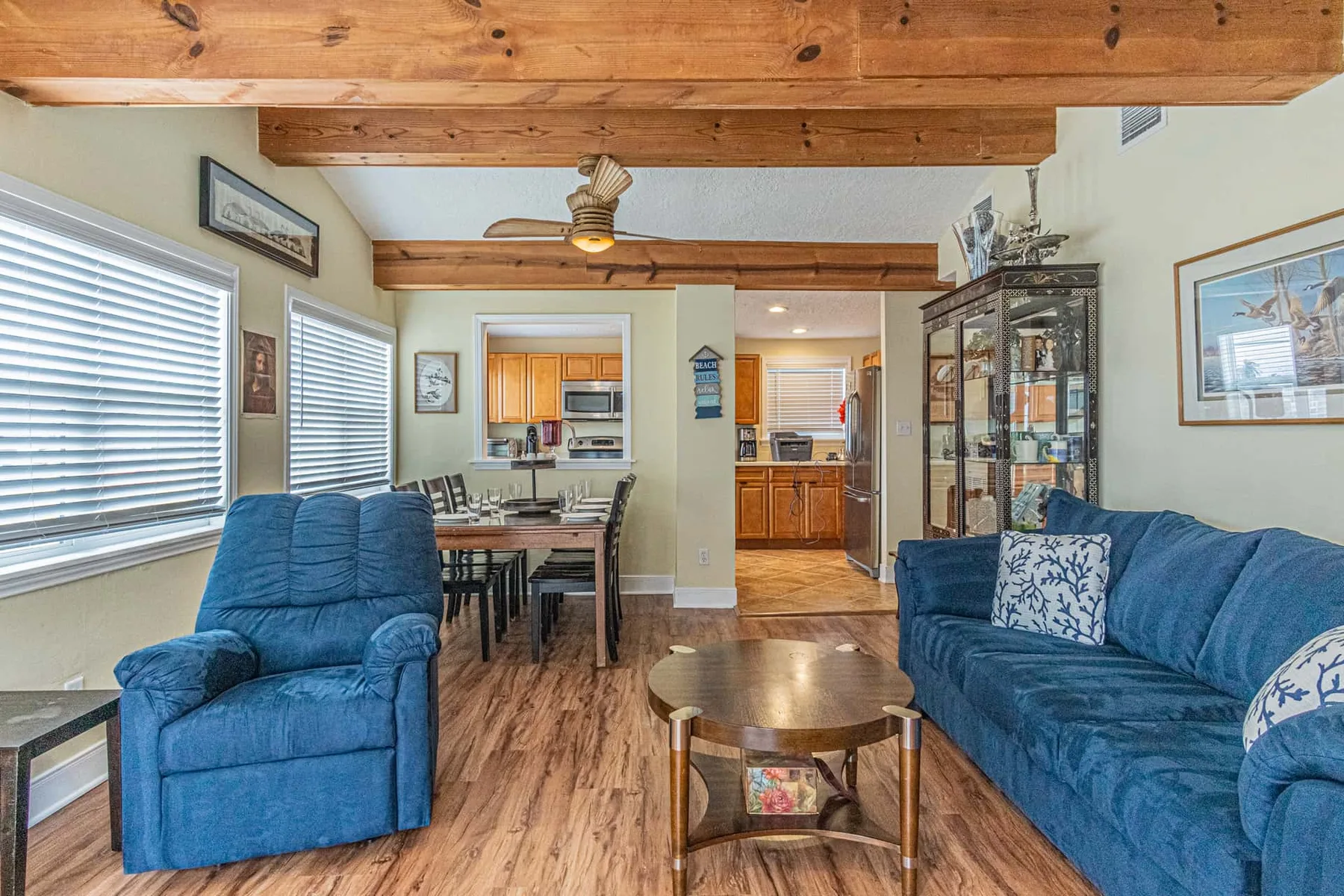 A living room with blue seating, a wooden coffee table, and exposed ceiling beams.