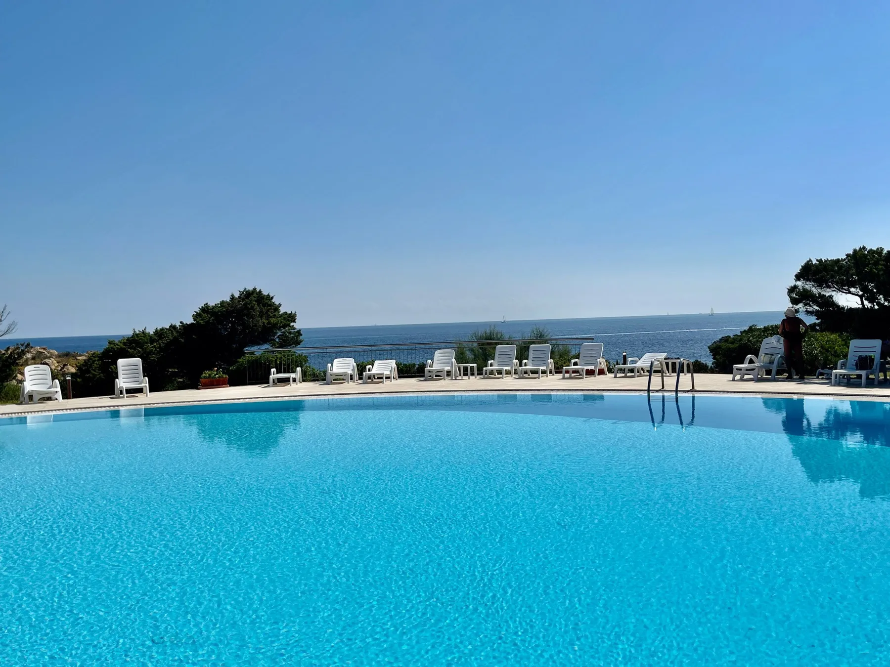 An outdoor swimming pool overlooks the sea, with lounge seating along the far edge.