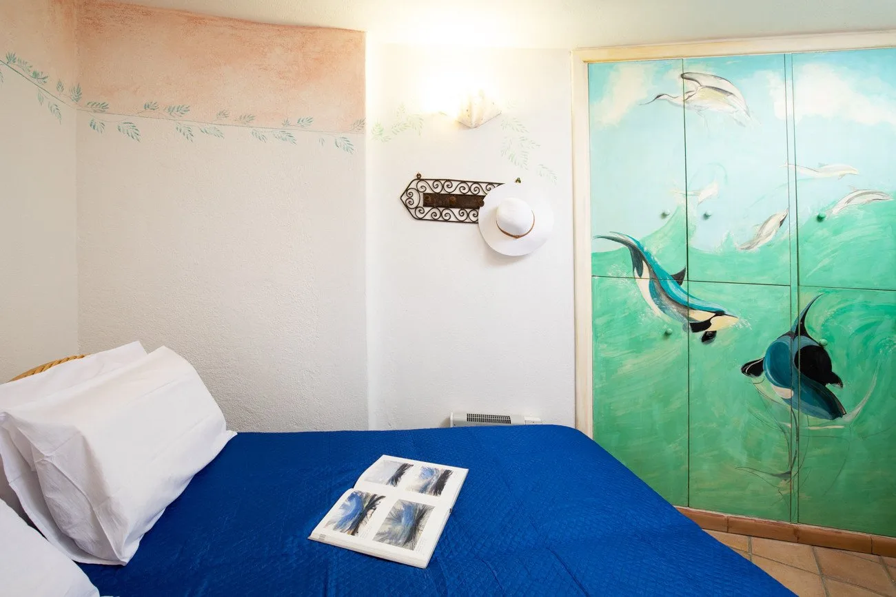 A bedroom with a bed covered in blue bedding and a painted wardrobe.