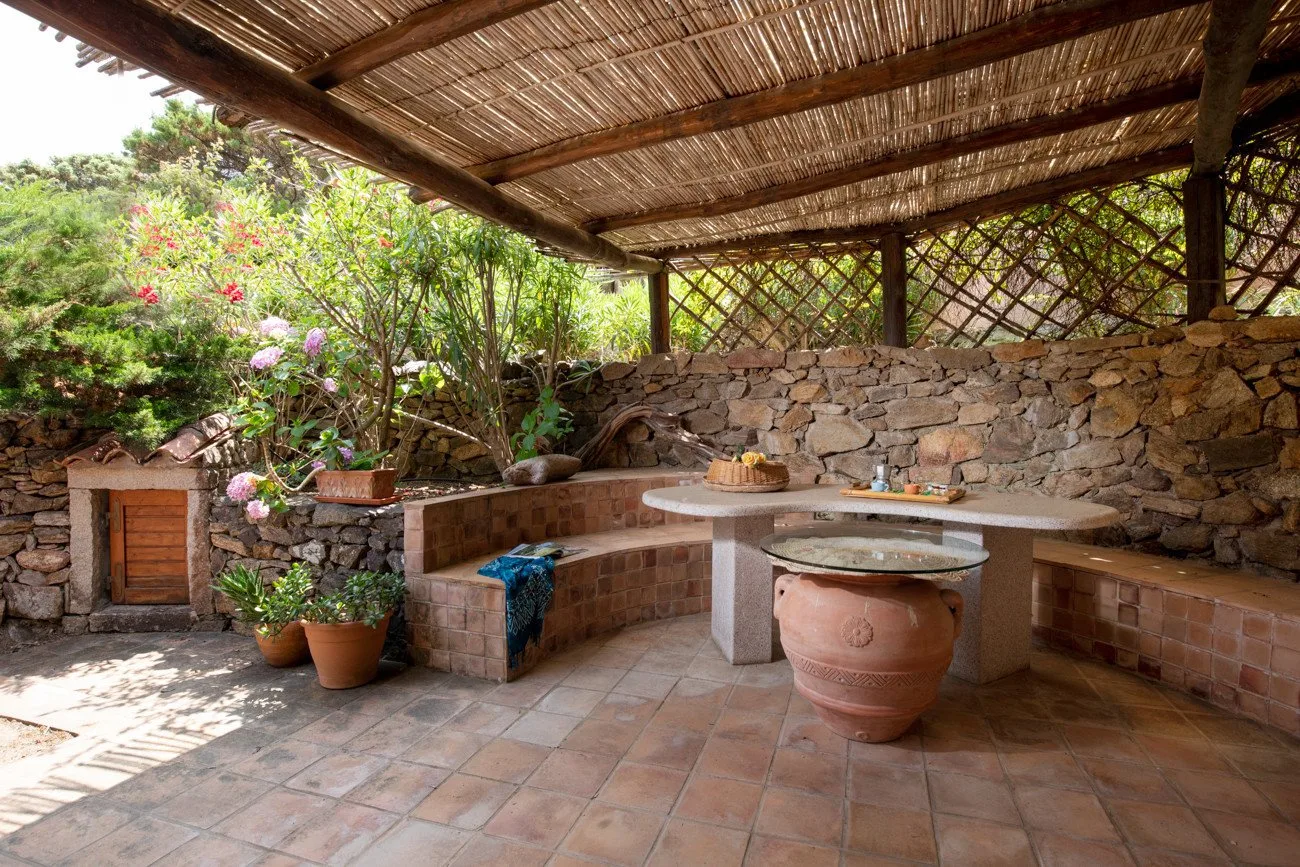 A covered outdoor patio with a tiled floor, stone walls, and built-in seating.