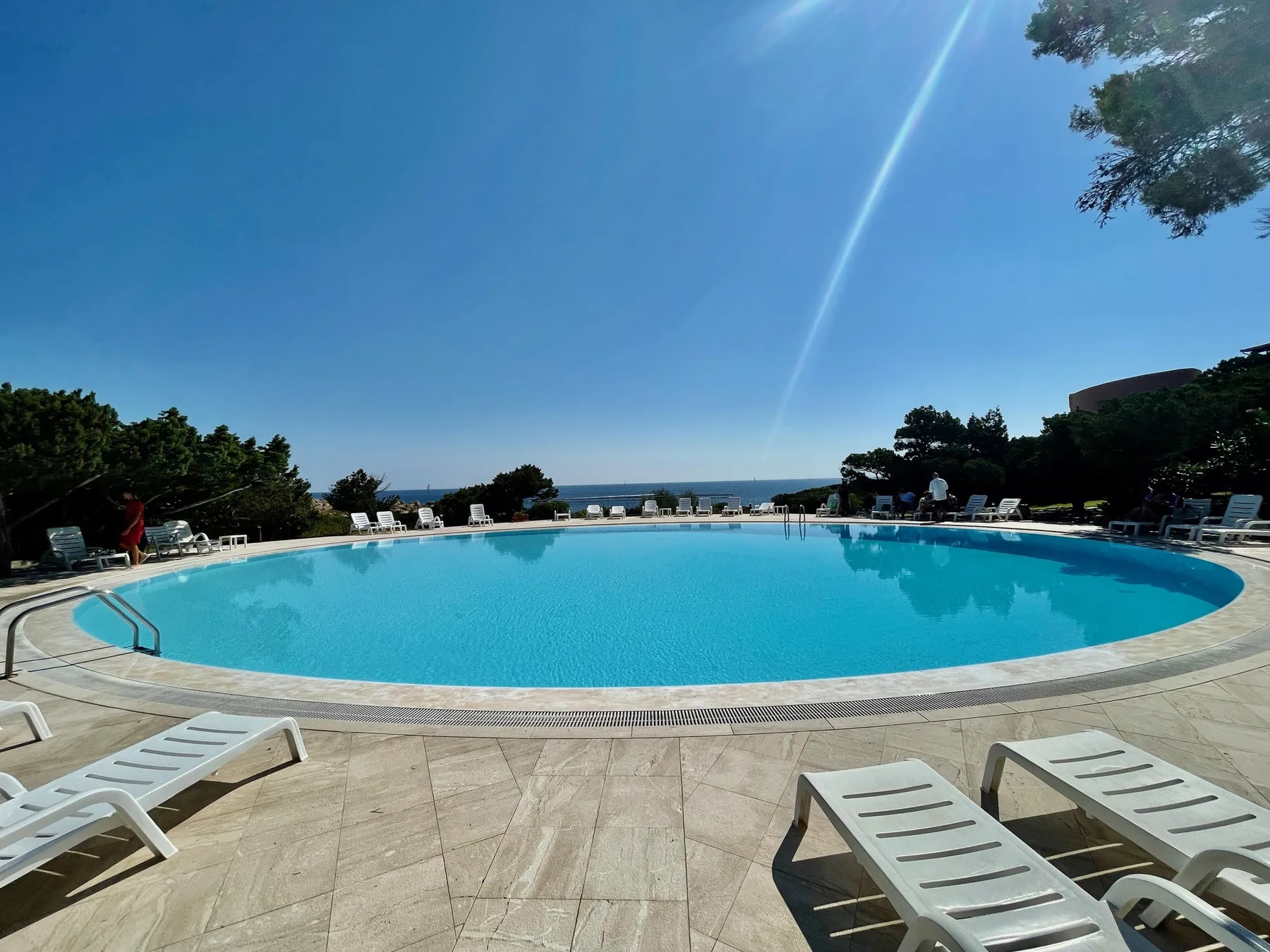 A large outdoor swimming pool overlooks the sea, with loungers arranged around its edge.