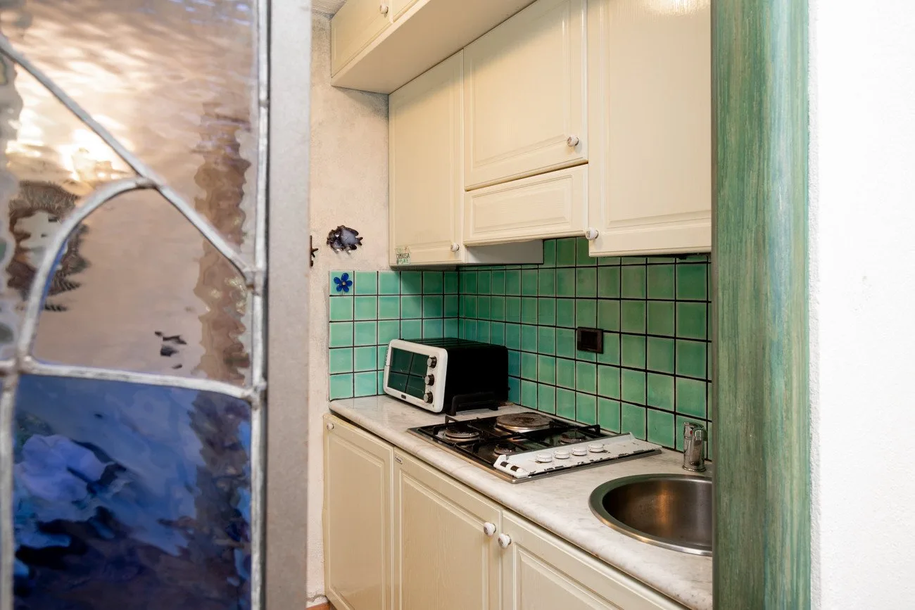A compact kitchen with cream cabinets, green tile, and a countertop stove.
