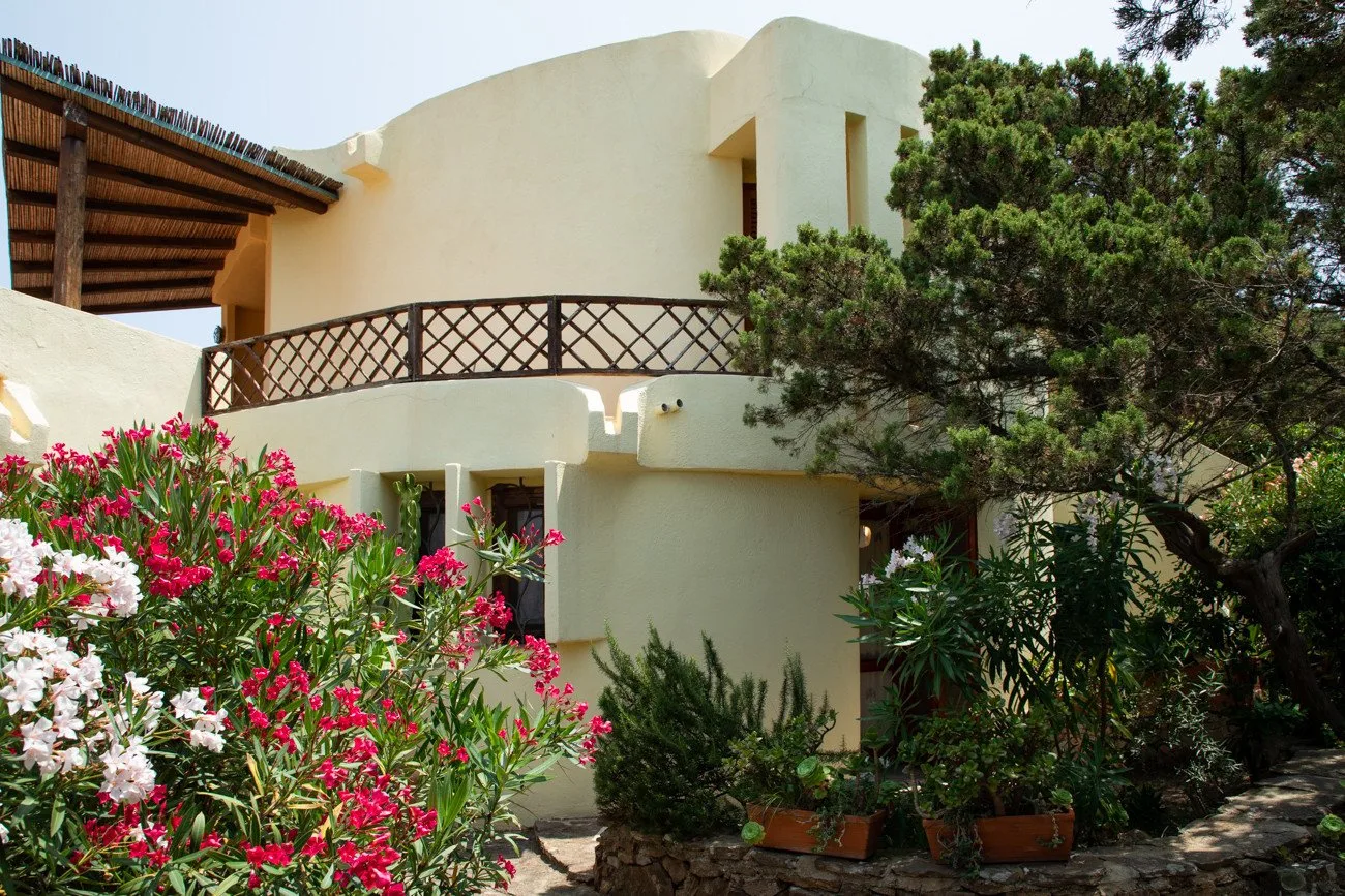A light-colored building stands among flowering shrubs and trees.